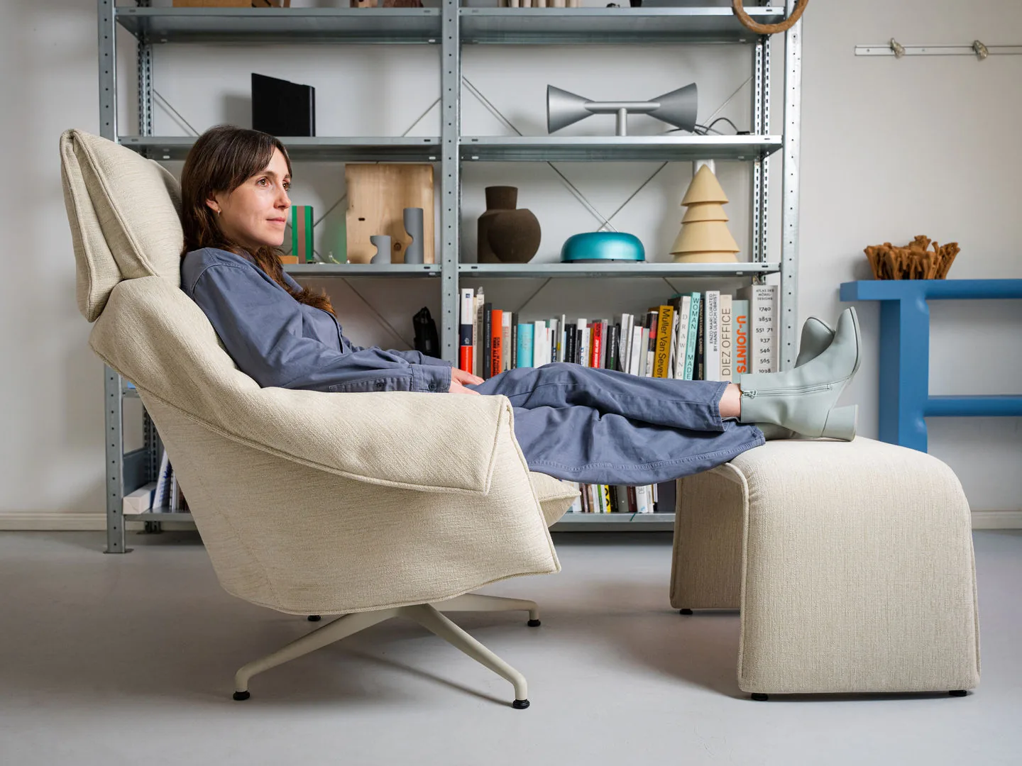 Vitra Loungesessel Bascule Highback mit Ottomane, zurückgelehnt, in einem Raum mit offenem Regal